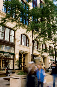 Blurred people walk past an urban Barnes & Noble retailer. Thin, deciduous trees stand in front of the store.