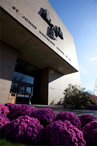 Angled view of the School of Law entryway. Purple shrubs line the path leading to the building.