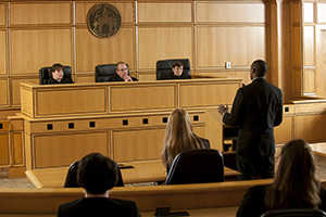 A man speaks in front of a bench of judges in a mock courtroom.