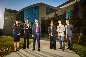Six people wearing suits pose in front of the law school.