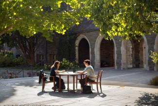 Students studying at outdoor table in front of the stone archways of Myron Taylor Hall.