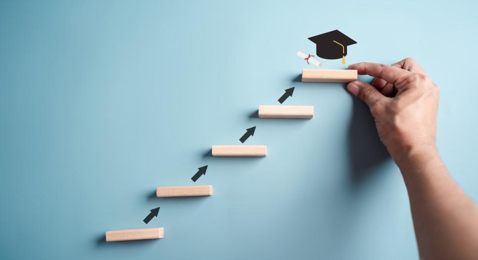 Representation of steps to graduation on a wall with a hand and graduation cap at the top step