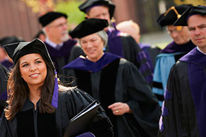 Graduates in black robes with purple accents walking.