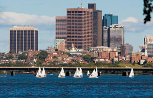 View of Boston. In the foreground, sailboats on the water. In the background, a cityscape with skyscrapers.