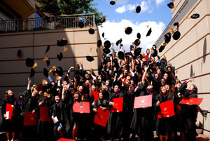 Graduates holding red diplomas toss their caps.