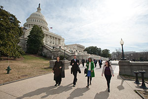 People walk down a sidewalk in front of the United States Capitol.