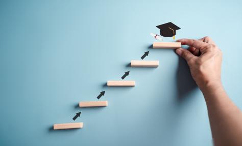 Representation of steps to graduation on a wall with a hand and graduation cap at the top step