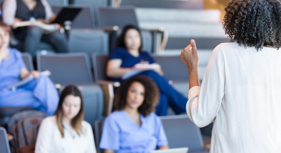 Students sitting in a classroom while a teacher presents. 