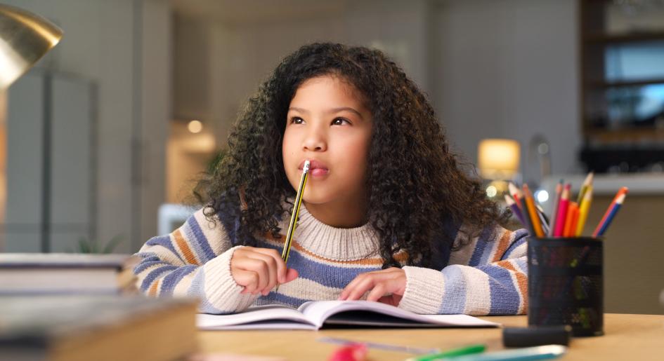 A young girl puts a pencil to her mouth in a pensive manner