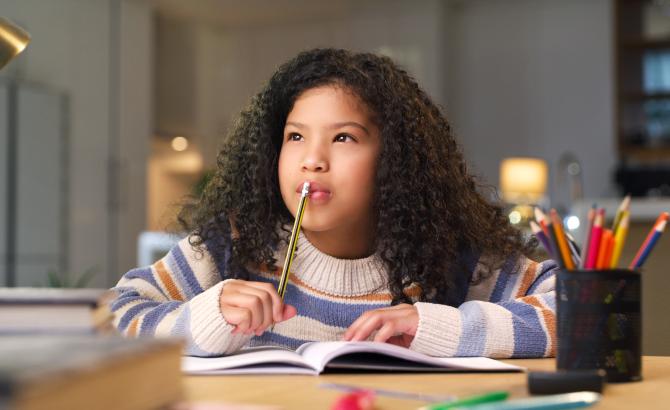 A young girl puts a pencil to her mouth in a pensive manner